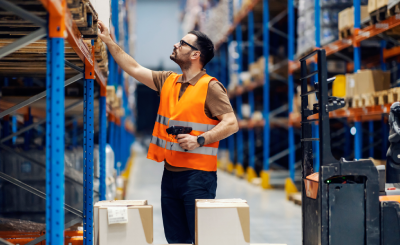 Worker checking inventory in a warehouse while wearing safety gear.